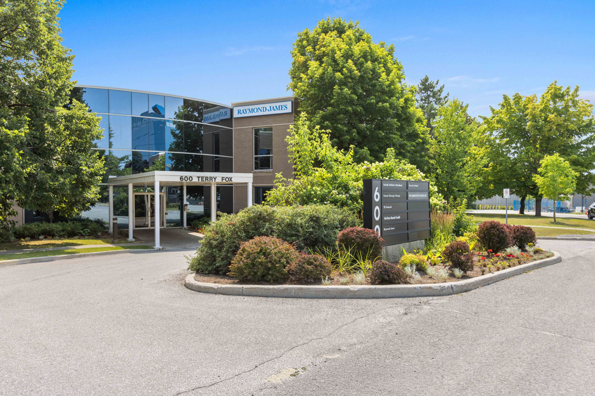Office building exterior with a landscaped entrance, circular driveway, and sign near the main entrance.