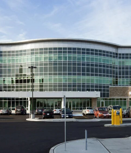 Exterior view of a large curved glass-front building with a parking lot in front.
