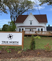 Exterior view of a white clinic building with a lawn and a True North Psychological Services sign in front in Dartmouth.