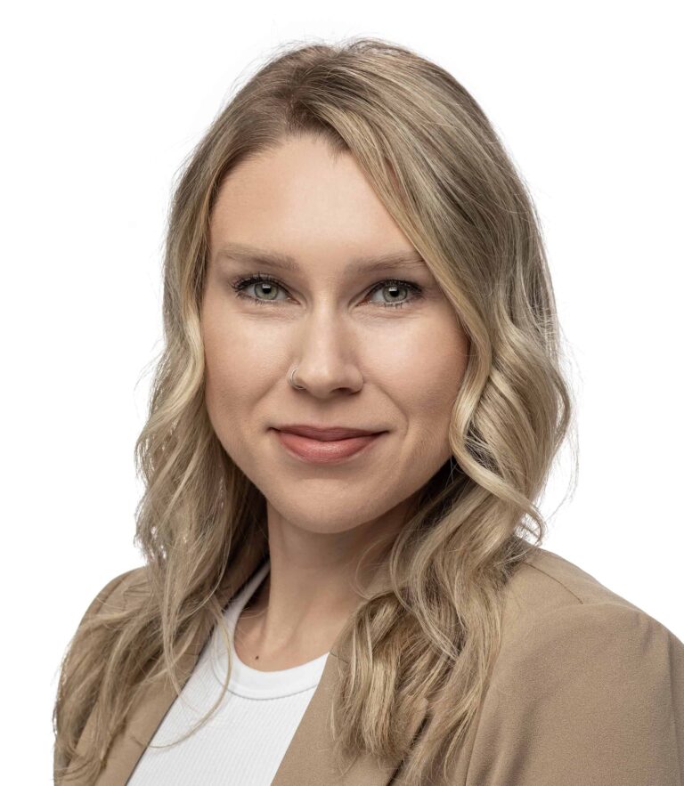 Person with wavy blonde hair wearing a tan blazer over a white top against a white background.