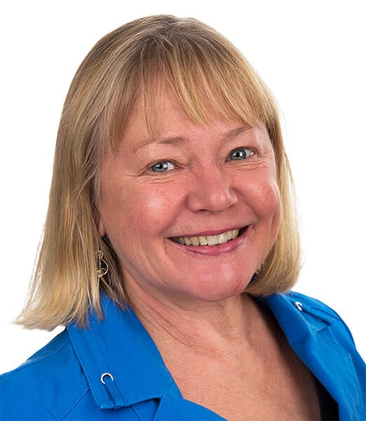 Smiling person with blonde hair wearing a blue jacket against a white background.