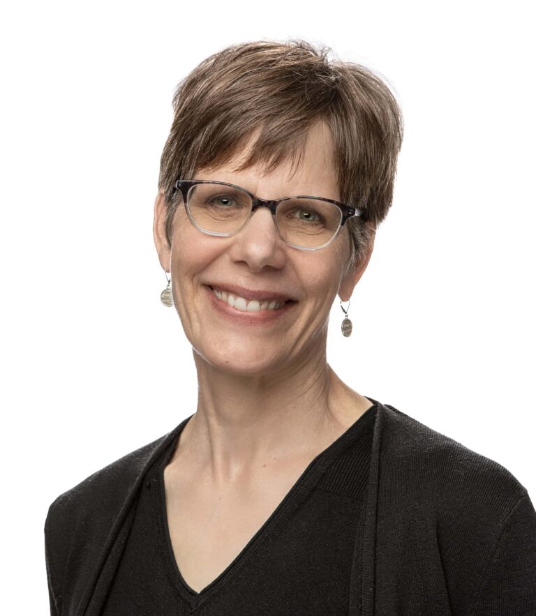 Smiling person with glasses wearing a black cardigan against a white background.
