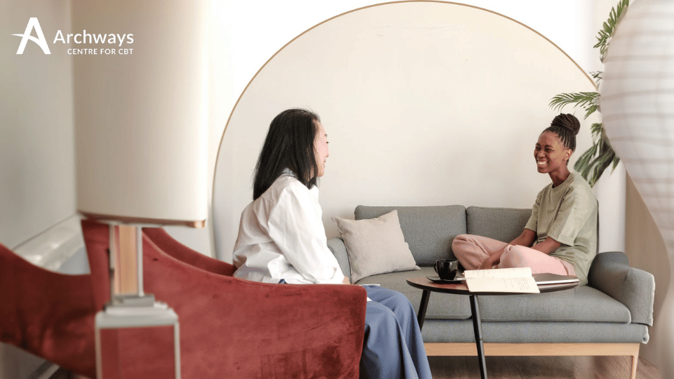 6548e677d4095889c2534e1f_Beige-Online-Counseling-Facebook-Post-Presentation Two people seated on couches facing each other in conversation.
