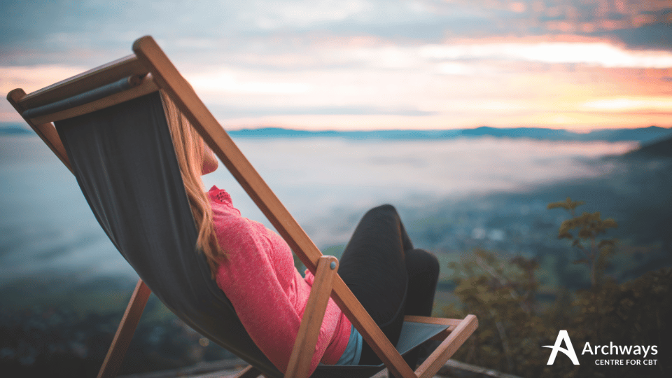 Person reclining in a deck chair overlooking a misty valley at sunset.