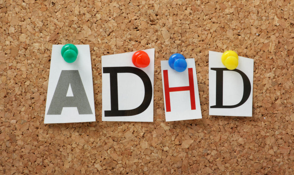 Letters spelling “ADHD” pinned to a corkboard with colorful pushpins.