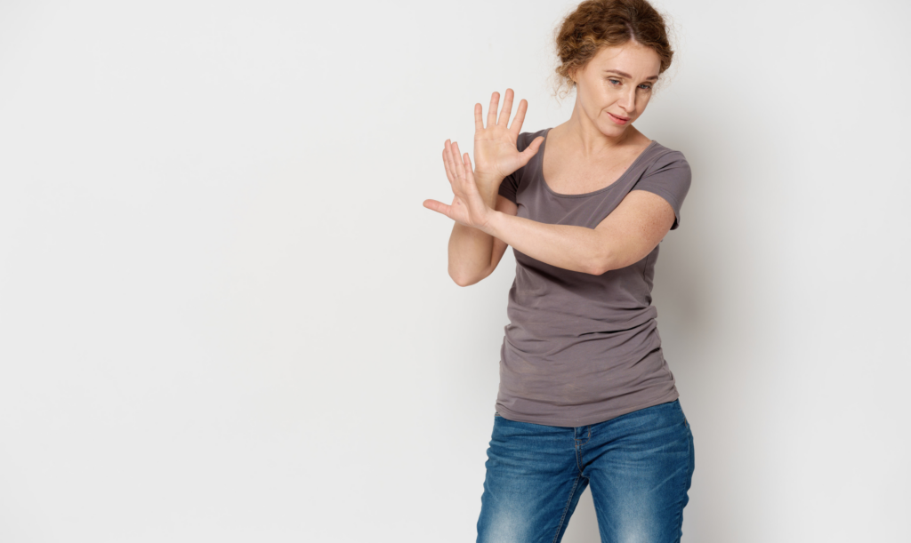 Person standing against a plain background with both hands raised in a stopping gesture.