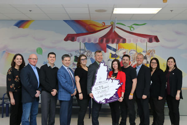Group of people standing indoors in front of a colorful mural, holding a large donation check.