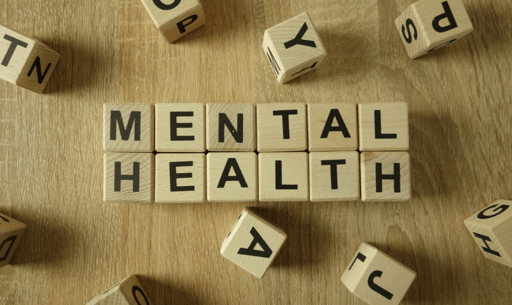 Wooden letter blocks spelling “MENTAL HEALTH” on a wooden surface.