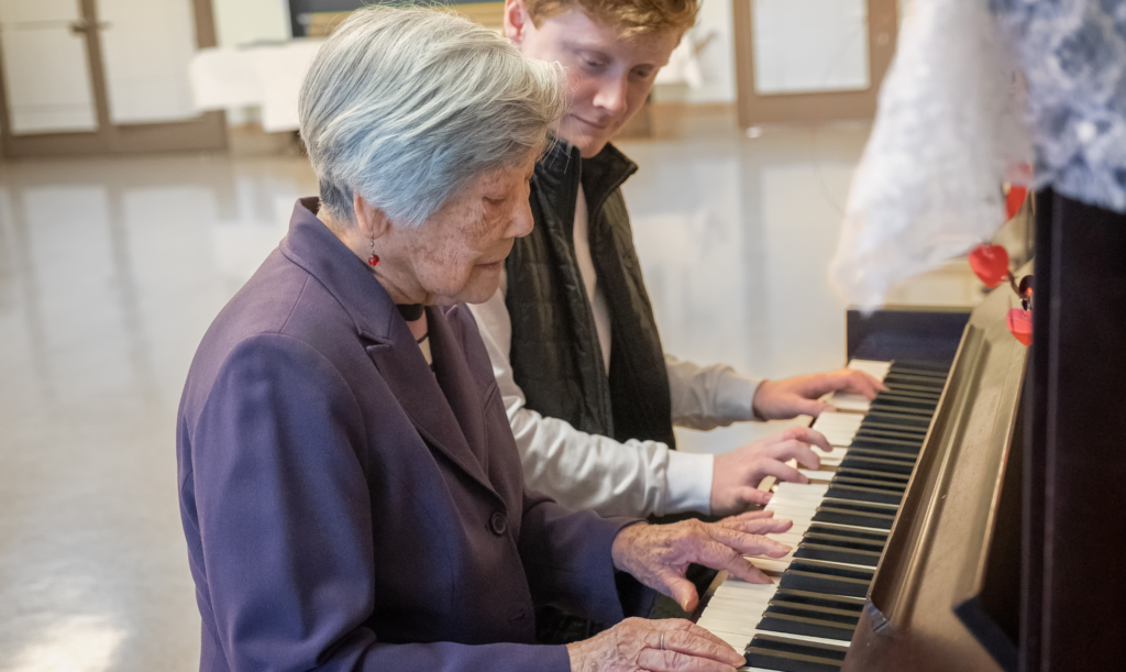 Older adult and younger person seated at a piano, playing side by side.