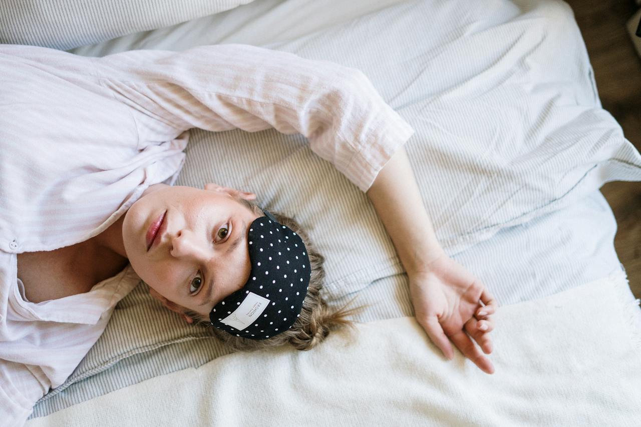Person lying on a bed with a sleep mask pushed up on their forehead.