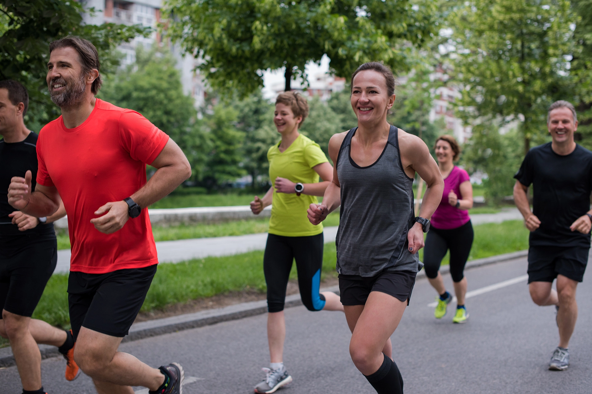 Group of adults jogging together on a paved path in a park.