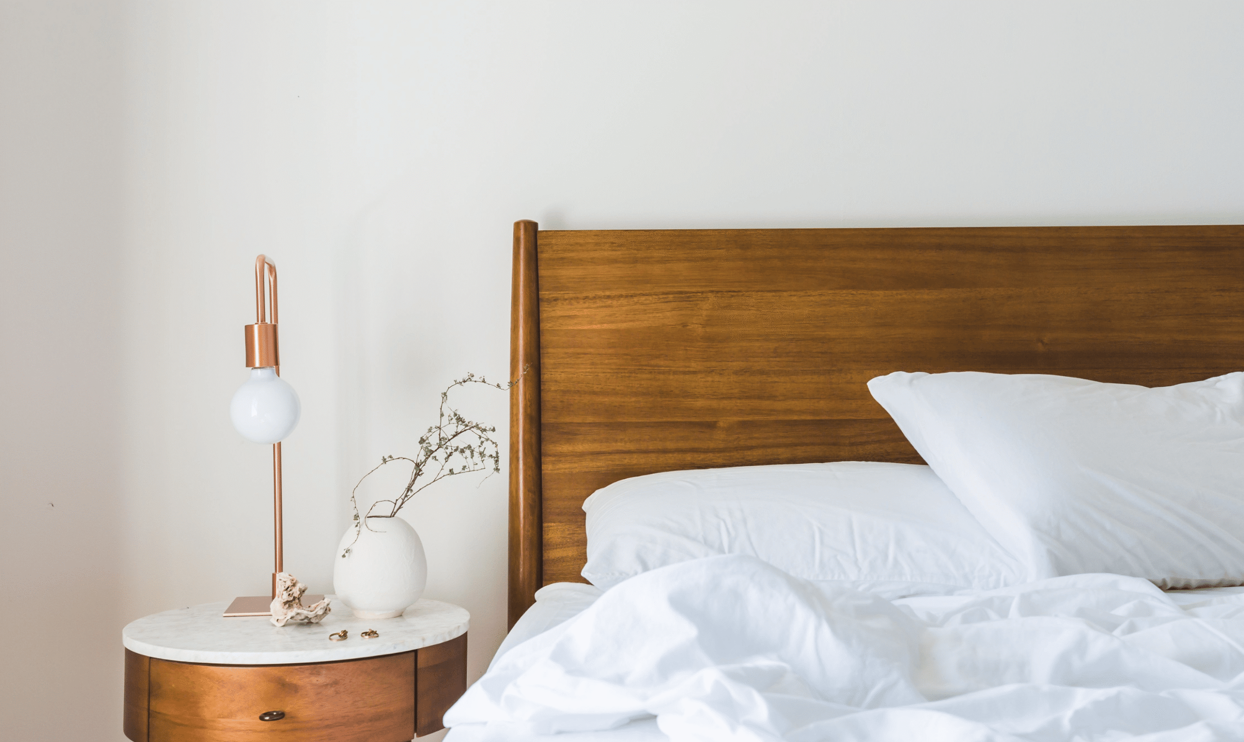 Unmade bed with white bedding, a wooden headboard, and a bedside table with a lamp.