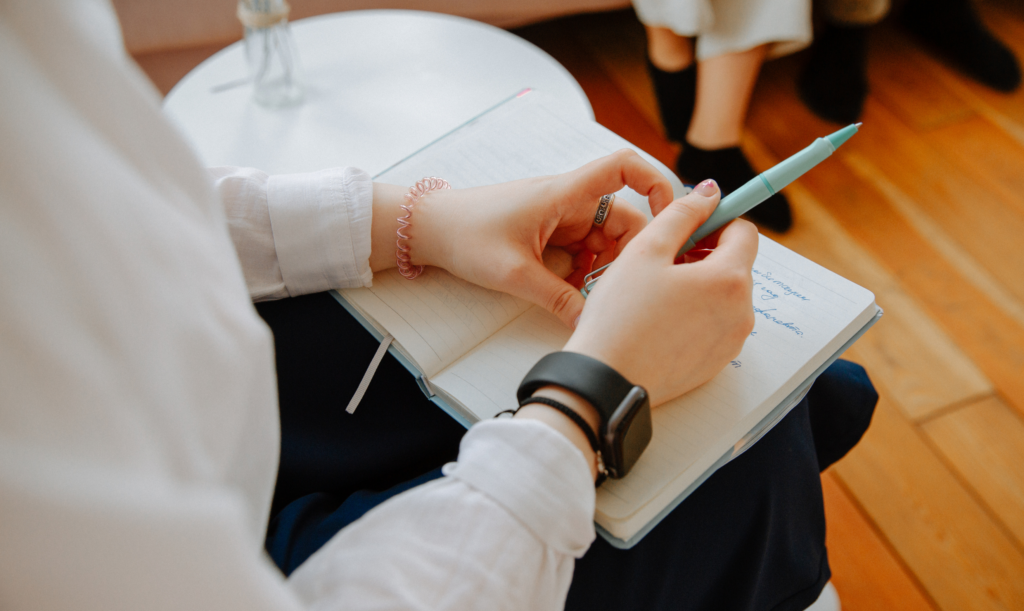 Close-up of hands holding a pen over an open notebook during a seated session.