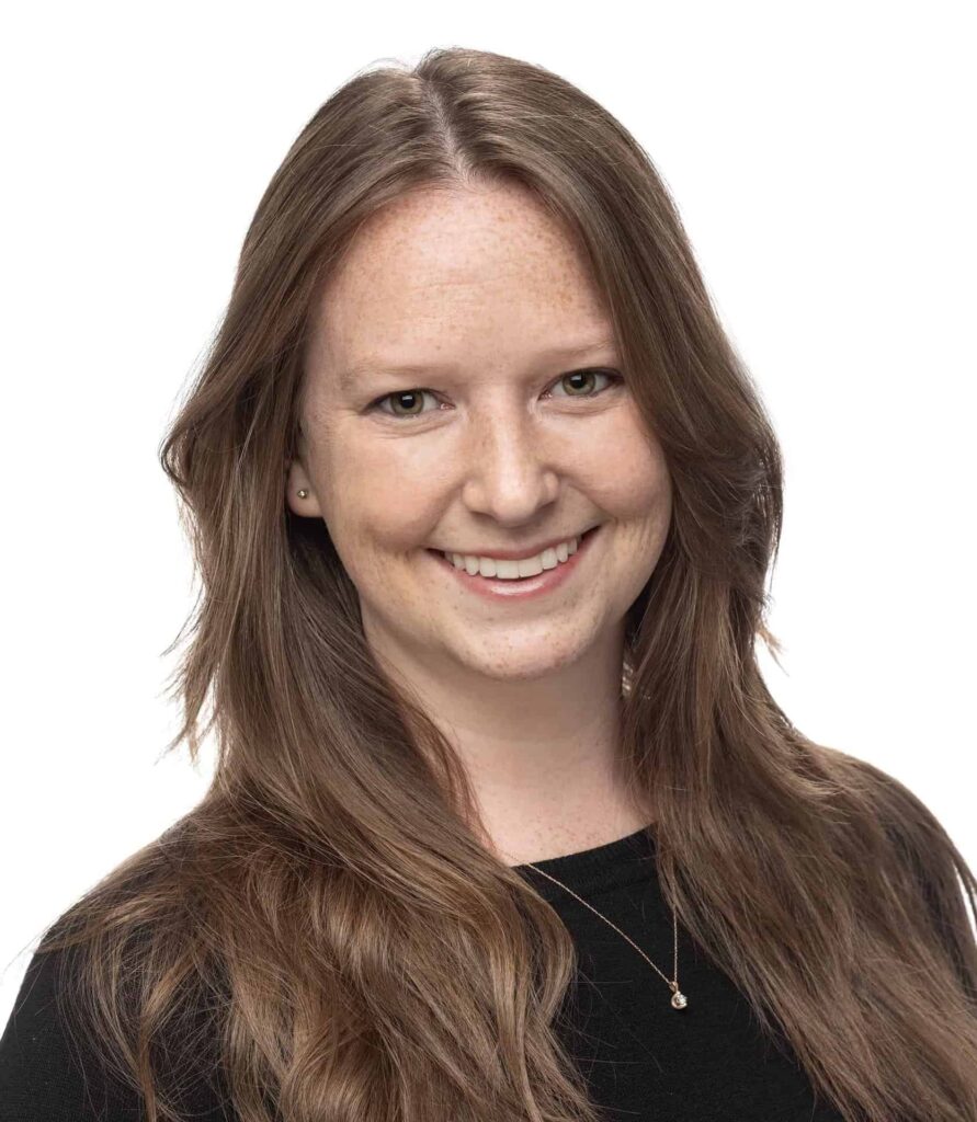 Smiling person with long brown hair wearing a black top against a white background.