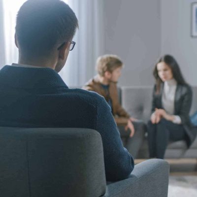Unfocused Couple on Counseling Session with Psychotherapist. Focus on Back of Therapist Taking Notes and Talking: People Sitting on Analyst Couch, Discussing Psychological and Relationship Problems